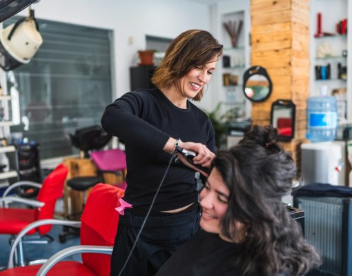 Hairdresser Smiling While Straightening Client’s Hair in a Modern Salon Hairdresser Smiling While Straightening Client's Hair in a Modern Salon