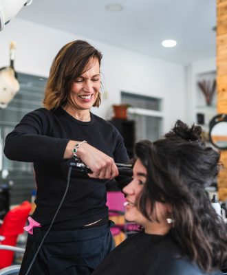 Smiling Hairdresser Straightening Client’s Hair in a Bright Salon Smiling Hairdresser Straightening Client's Hair in a Bright Salon